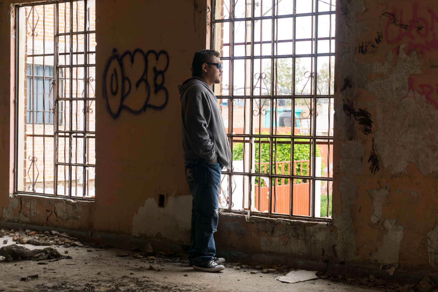 El Mijis stands in an abandoned building of Ciudad 2000 neighborhood. The Zetas cartel occupied this district and the shopkeepers had to escape. After this cartel was pushed out the city, these buildings are now empty. El Mijis was elected for this district of the city of San Luis Potosi and he wants a normal life to come back. 
Col. Ciudad 2000, San Luis Potosi, SLP, Mexico - 05/12/2015.

El Mijis regarde par la fenêtre d'un bâtiment abandonné du quartier de la Ciudad 2000. Le cartel des Zetas a occupé ce quartier et les commerçants n'avaient d'autre choix que de fuir. Après que ce cartel fut chassé de la ville, ces bâtiments sont restés vides. El Mijis a été élu notamment pour ce district et espère y faire retrouver une vie normale.
Col. Ciudad 2000, San Luis Potosi, SLP, Mexique - 05/12/2015.