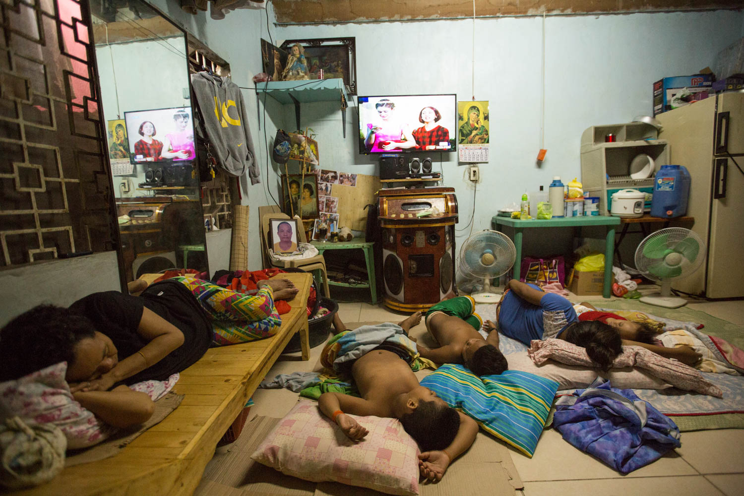 Baseco is an informal neighborhood of Manila located between the international port and the Pasig river. More than 50 000 people are living there in very precarious conditions. 
All the family got sleeping watching the TV. On a chair on the left of the screen is a picture of the father, who got shot in his shop getting stolen the cash. 
Manila, Philippines - 13/01/2016.