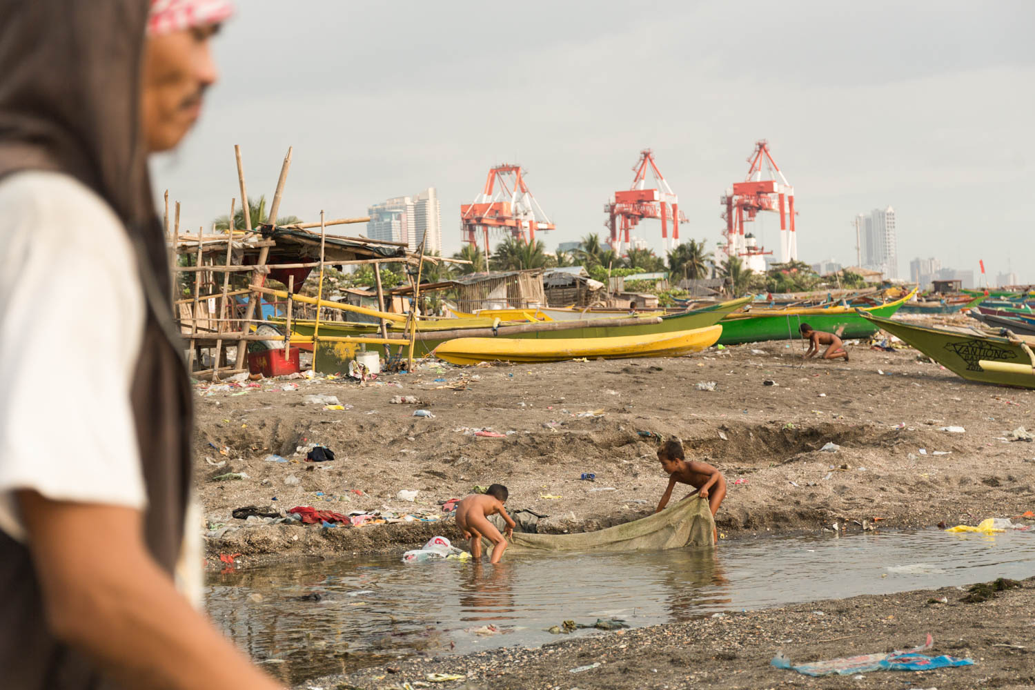Baseco is an informal neighborhood of Manila located between the international port and the Pasig river. More than 50 000 people are living there in very precarious conditions.  The beach is a very active place. Mens are going to fish, others maintaining their boats or fish nets. Children are playing to catch fishes or digging holes in the sand. Manila, Philippines - 13/01/2016.
