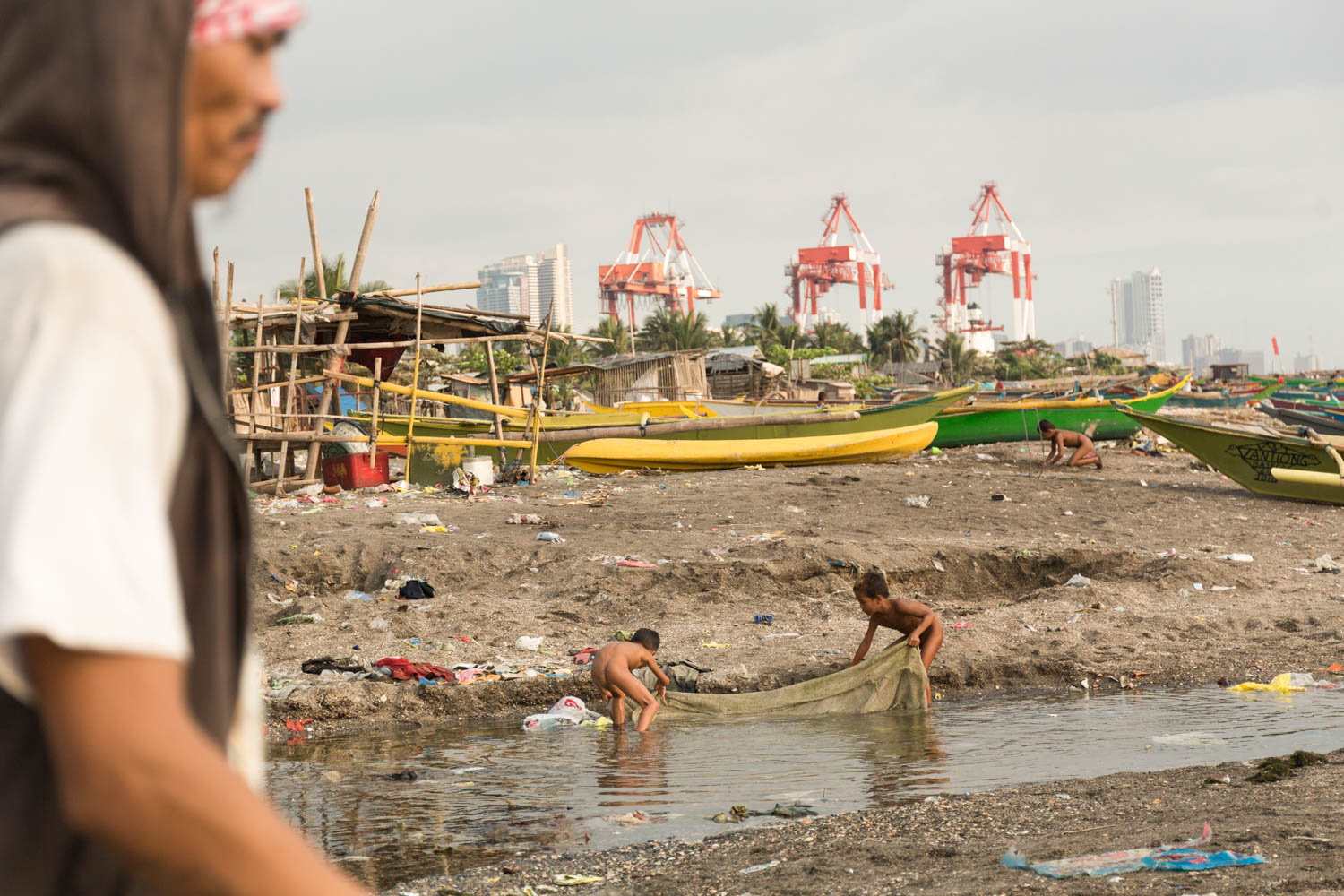 Baseco is an informal neighborhood of Manila located between the international port and the Pasig river. More than 50 000 people are living there in very precarious conditions.  
The beach is a very active place. Mens are going to fish, others maintaining their boats or fish nets. Children are playing to catch fishes or digging holes in the sand. 
Manila, Philippines - 13/01/2016.