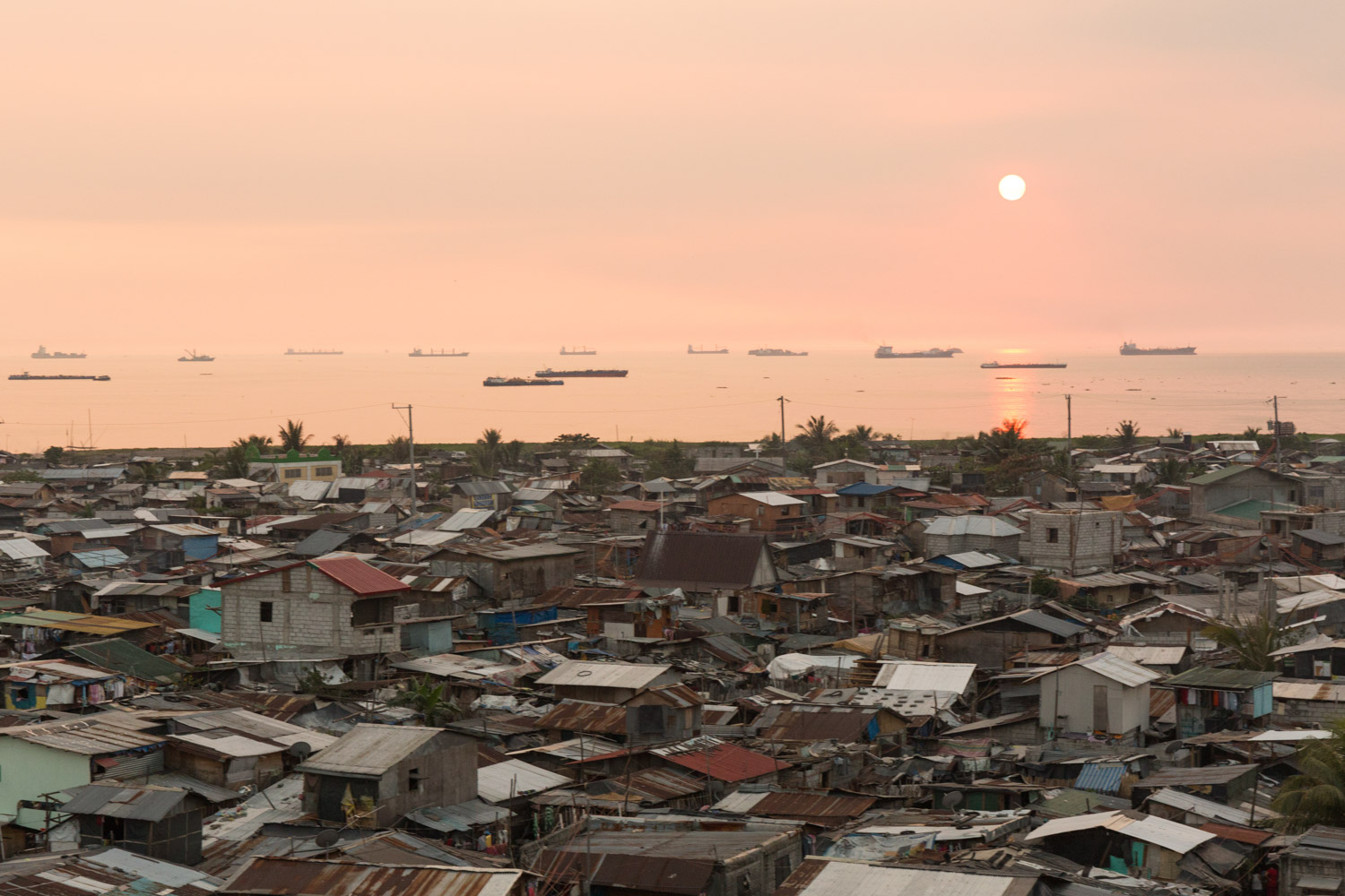 Baseco is an informal neighborhood of Manila located between the international port and the Pasig river. More than 50 000 people are living there in very precarious conditions.  
Sunset on Baseco and Manila bay. Many boats are waiting to enter to the port. 
Manila, Philippines - 13/01/2016.