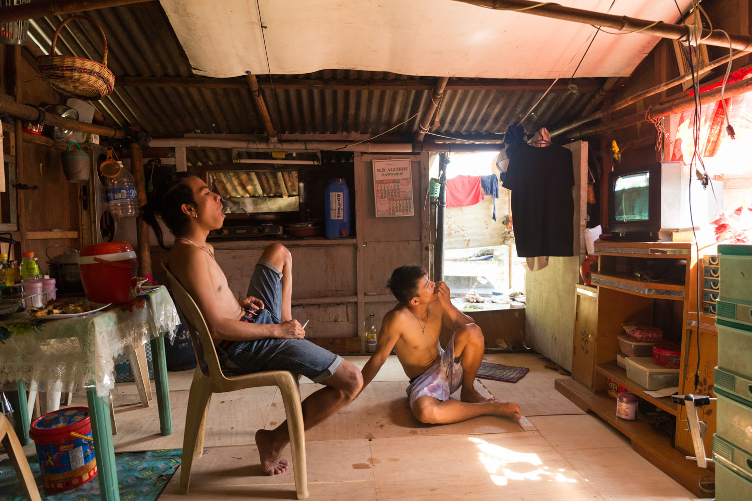 Eman and his friend Josh after eating the fishes caught in the morning are relaxing watching the TV. Buli, Muntinlupa, Metro Manila, Philippines - 12/01/2016.